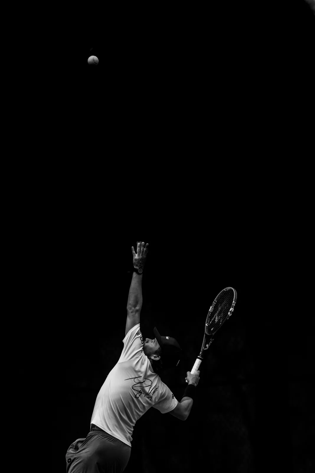 Miguel, in black and white, tosses the ball to serve against a black background.